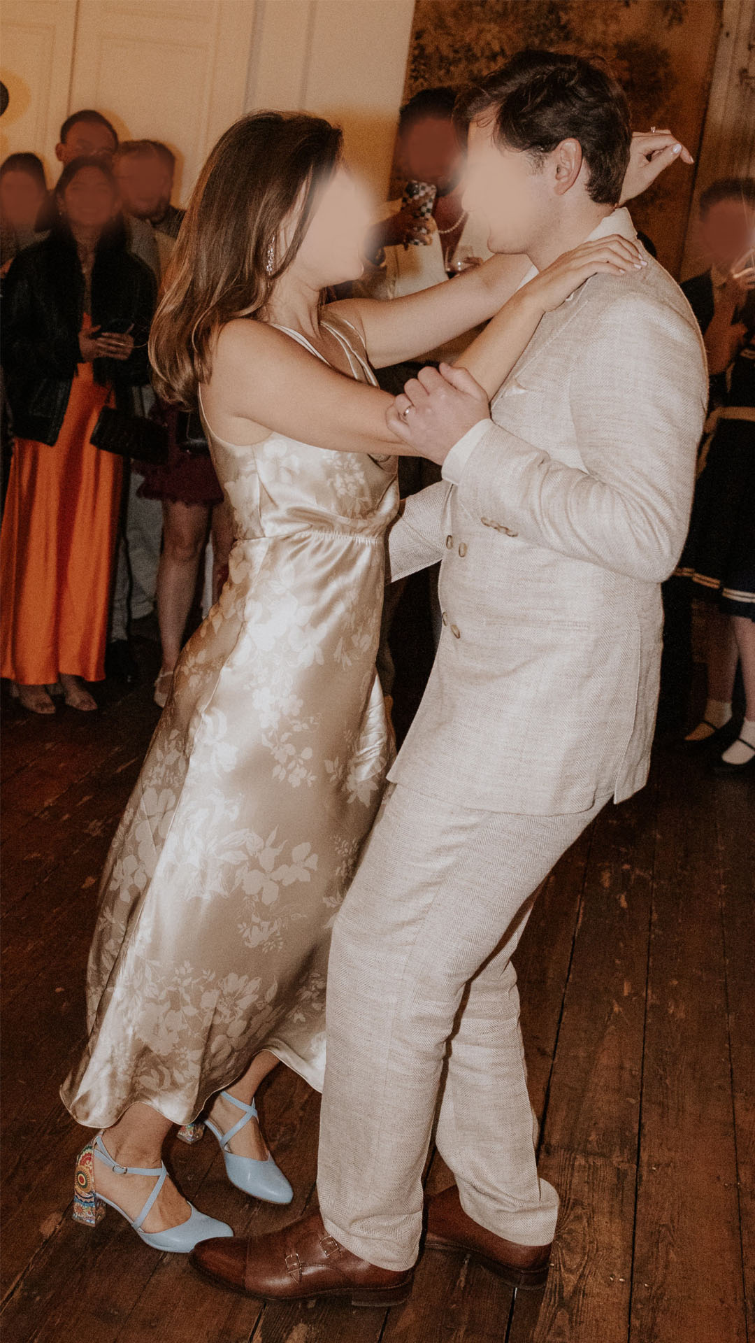 A bride and groom dancing together indoors; the bride's floral silk dress is fitted at the waist and bodice.